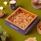 Gift box with shredded paper on a green surface with candles and decorative items.